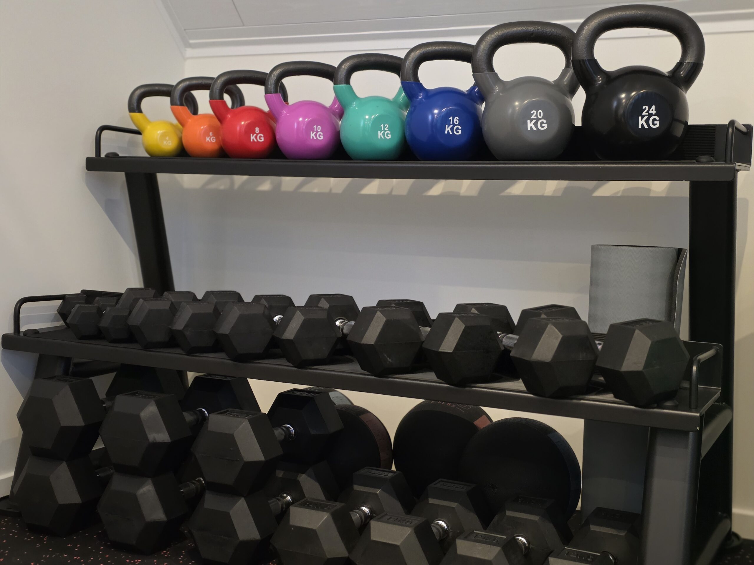 Rek met kleurrijke kettlebells en zwarte dumbbells in de privé fitness Level170, moderne trainingsruimte.